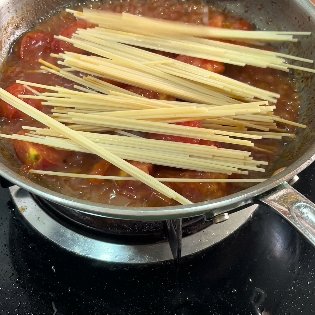Espaguetis largos sumergiéndose en la salsa de tomate dentro de la sartén.