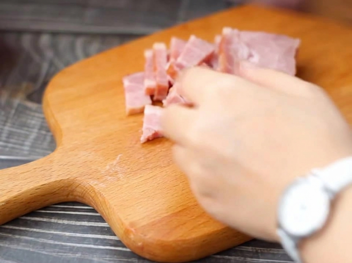 Tiras de tocino cortándose en trozos más pequeños sobre una tabla de cortar de madera.