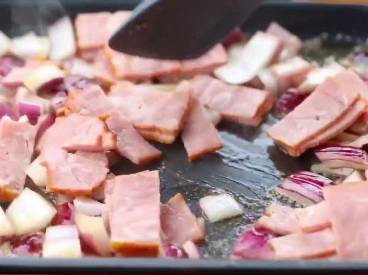 Tiras de tocino y cebollas picadas friéndose juntas en una sartén.
