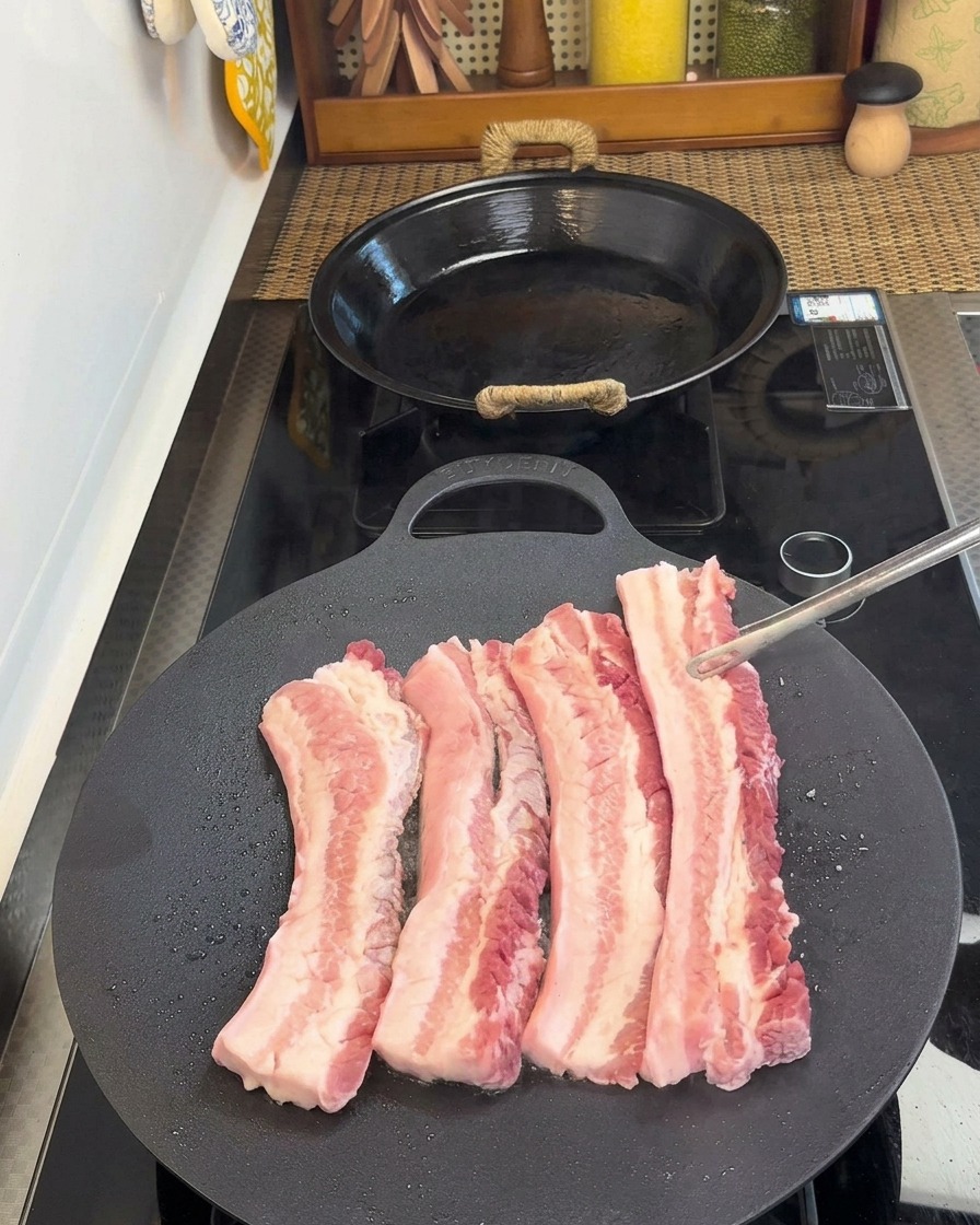 Pinzas volteando tiras de panceta en una sartén, revelando el lado cocinado y dorado.