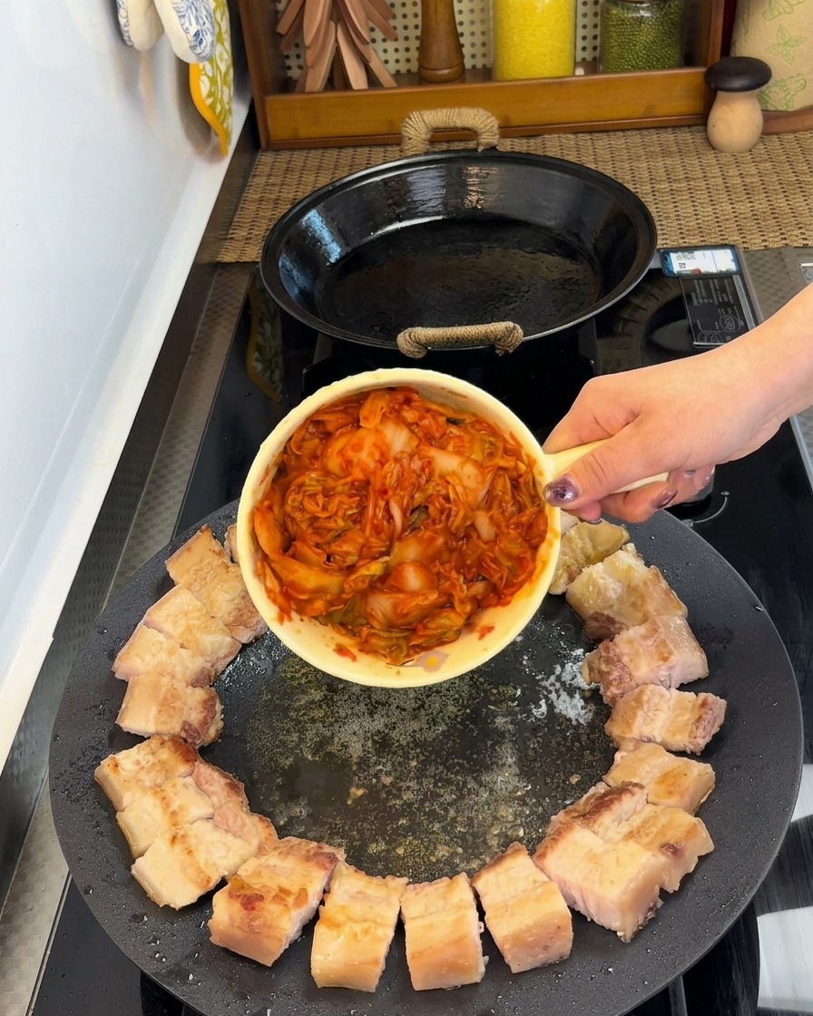 Trozos de panceta dispuestos en círculo con una porción de kimchi en el centro de la sartén.