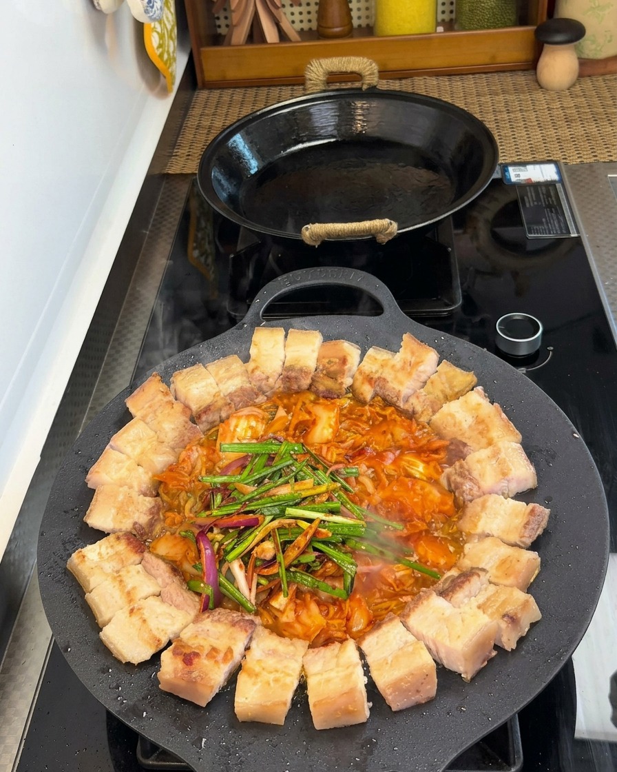 Panceta y kimchi en una sartén cubiertos con puerros frescos, cebollas y varios condimentos.