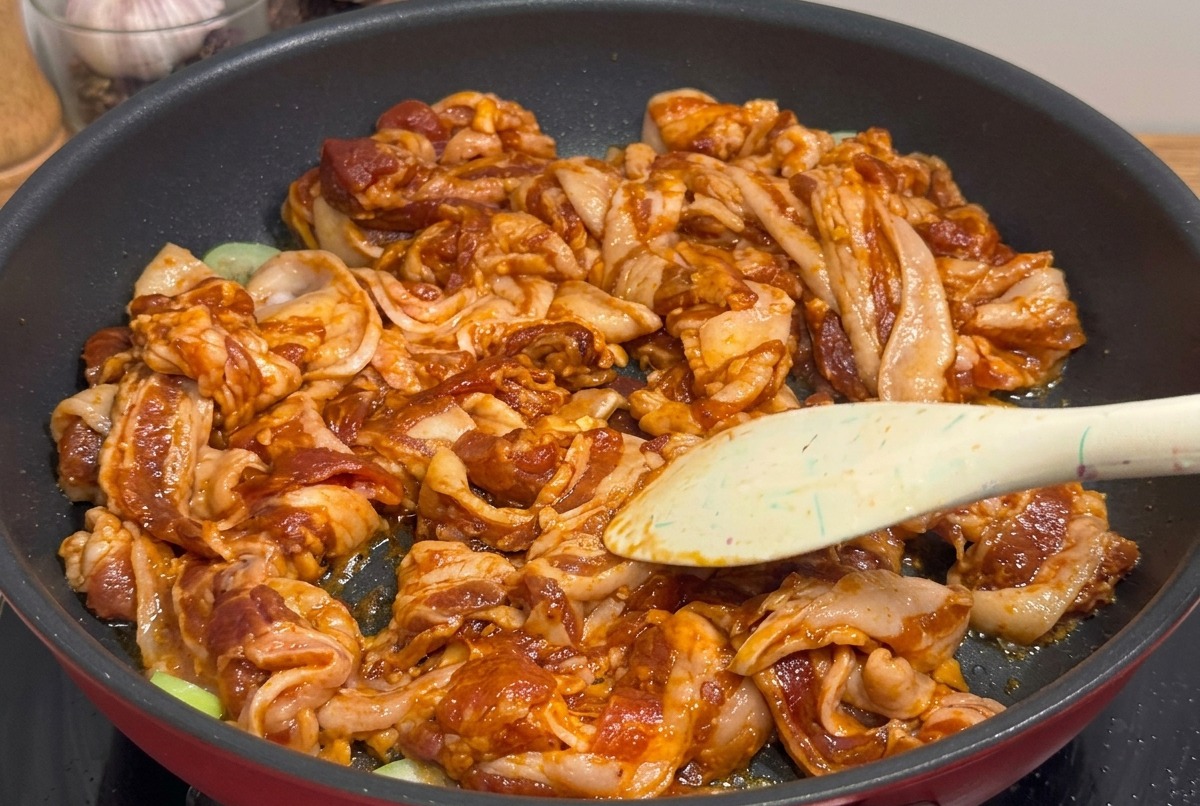 Trozos pequeños de panceta glaseada siendo cortados con tijeras de cocina directamente en la sartén.
