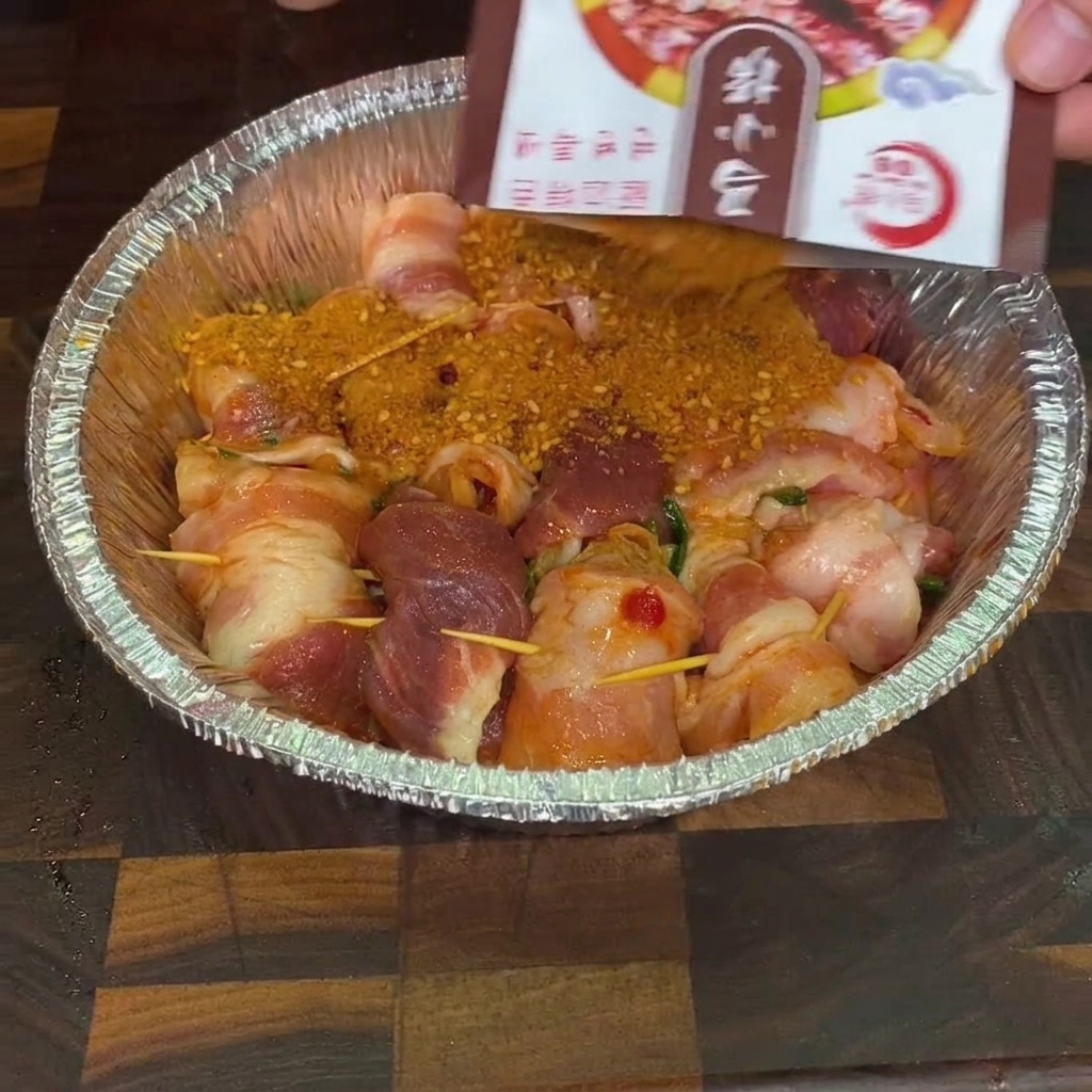 Sazonador para barbacoa siendo espolvoreado desde un sobre sobre rollitos de carne crudos en una bandeja de aluminio.
