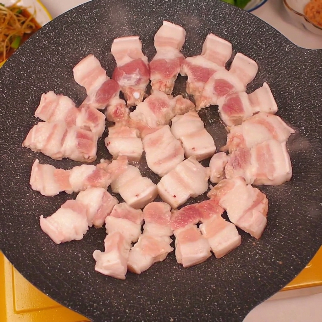 Láminas de panceta de cerdo dispuestas en círculo sobre una parrilla caliente.