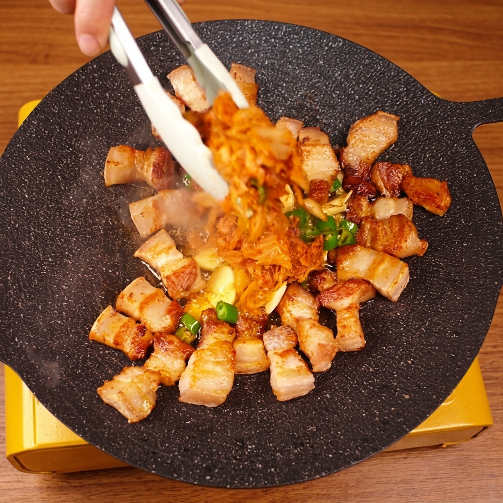 Uso de pinzas para mezclar la panceta y el kimchi sobre la plancha caliente.
