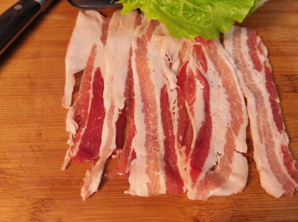 Una loncha de panceta con una hoja de lechuga, zanahoria, cebolla y kimchi, lista para enrollar.