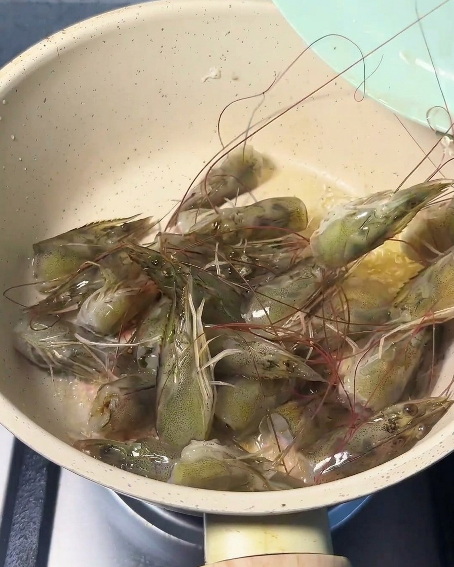 Cabezas de camarón frescas friéndose en una sartén con aceite, volviéndose rosadas y liberando su aroma.