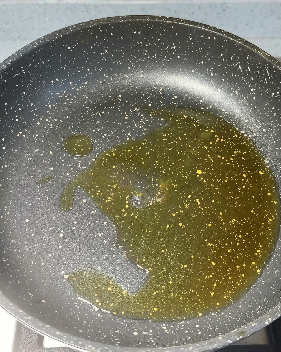 Ajo picado y pasta roja de camarón friéndose en aceite caliente en una sartén.