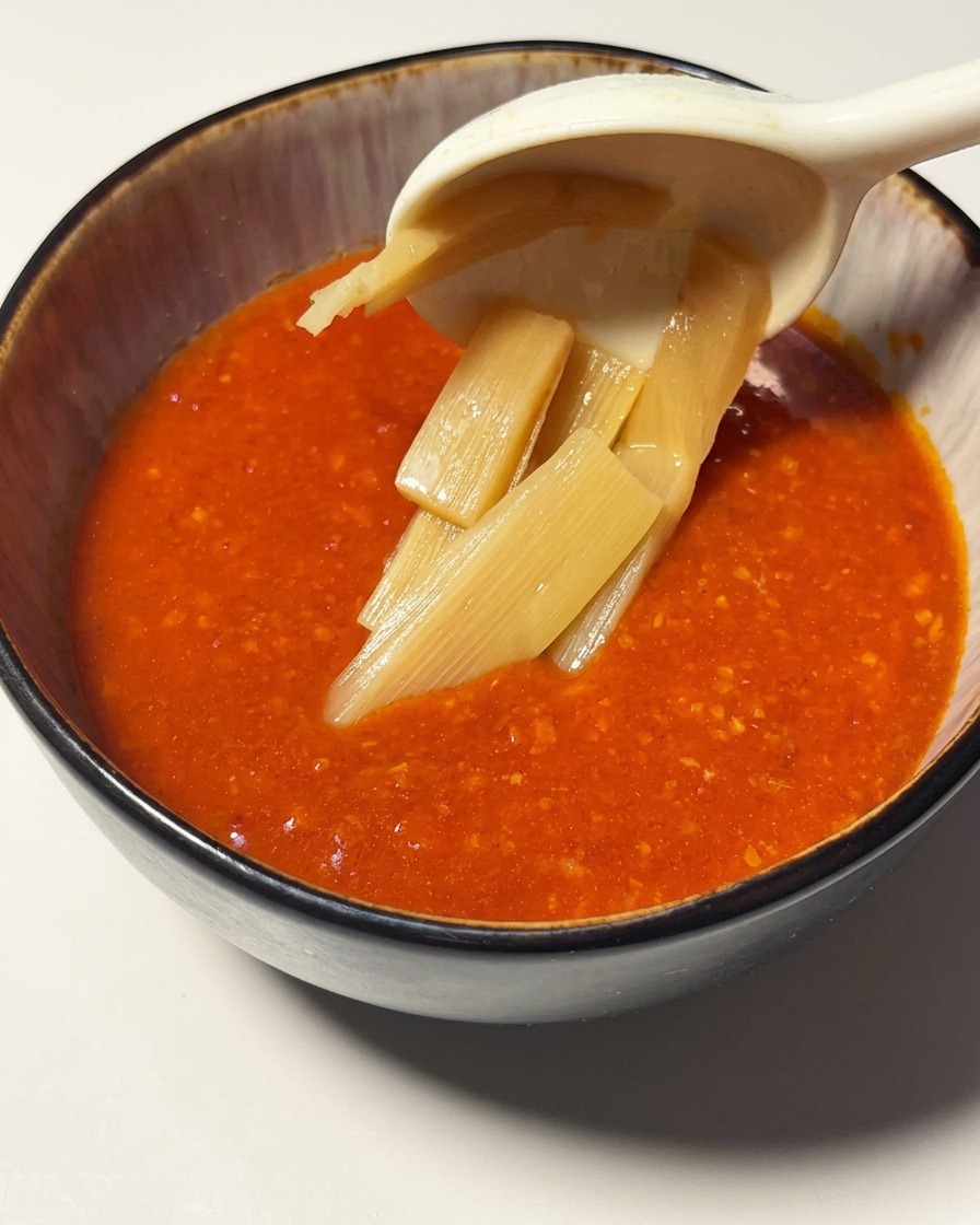 Rebanadas de brotes de bambú siendo levantadas con una cuchara en un tazón lleno de la vibrante salsa de tomate y camarón.