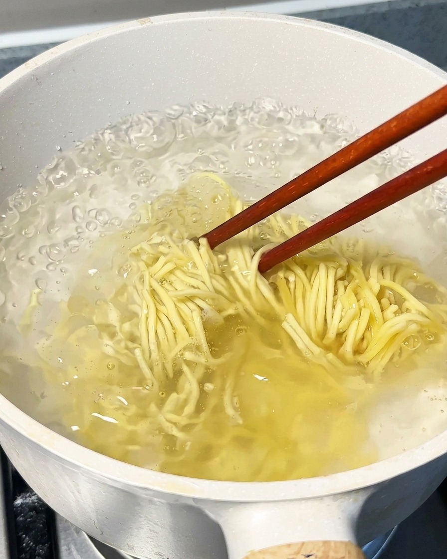 Fideos hirviendo en una olla grande con agua, siendo removidos con palillos de madera.