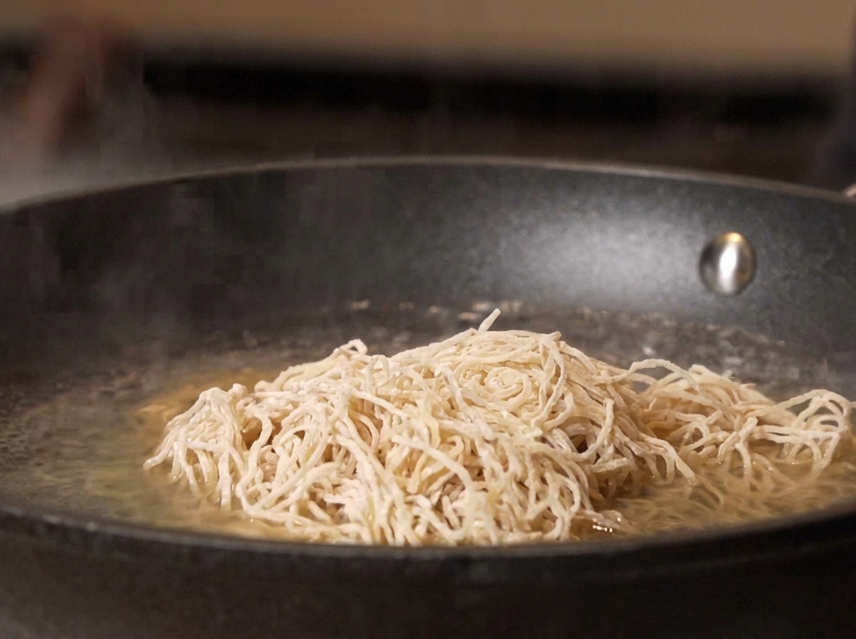 Fideos crudos cayendo en una olla con agua hirviendo.