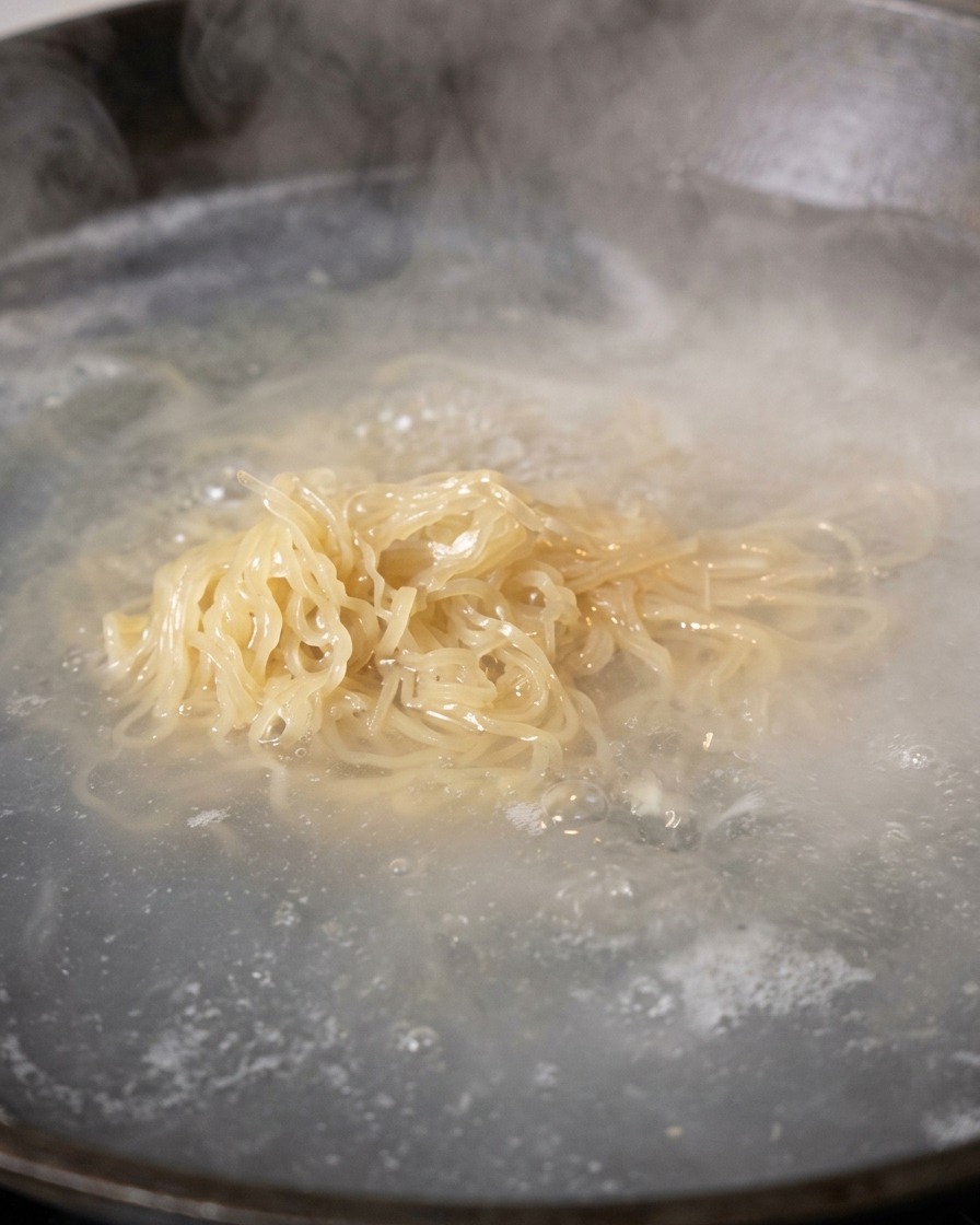 Fideos cocidos siendo retirados del agua hirviendo con unos palillos para escurrirse.