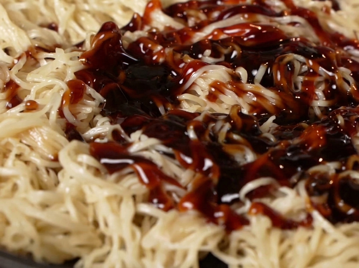 Salsa de ostras y salsa de soja vertiéndose sobre los fideos en la sartén.