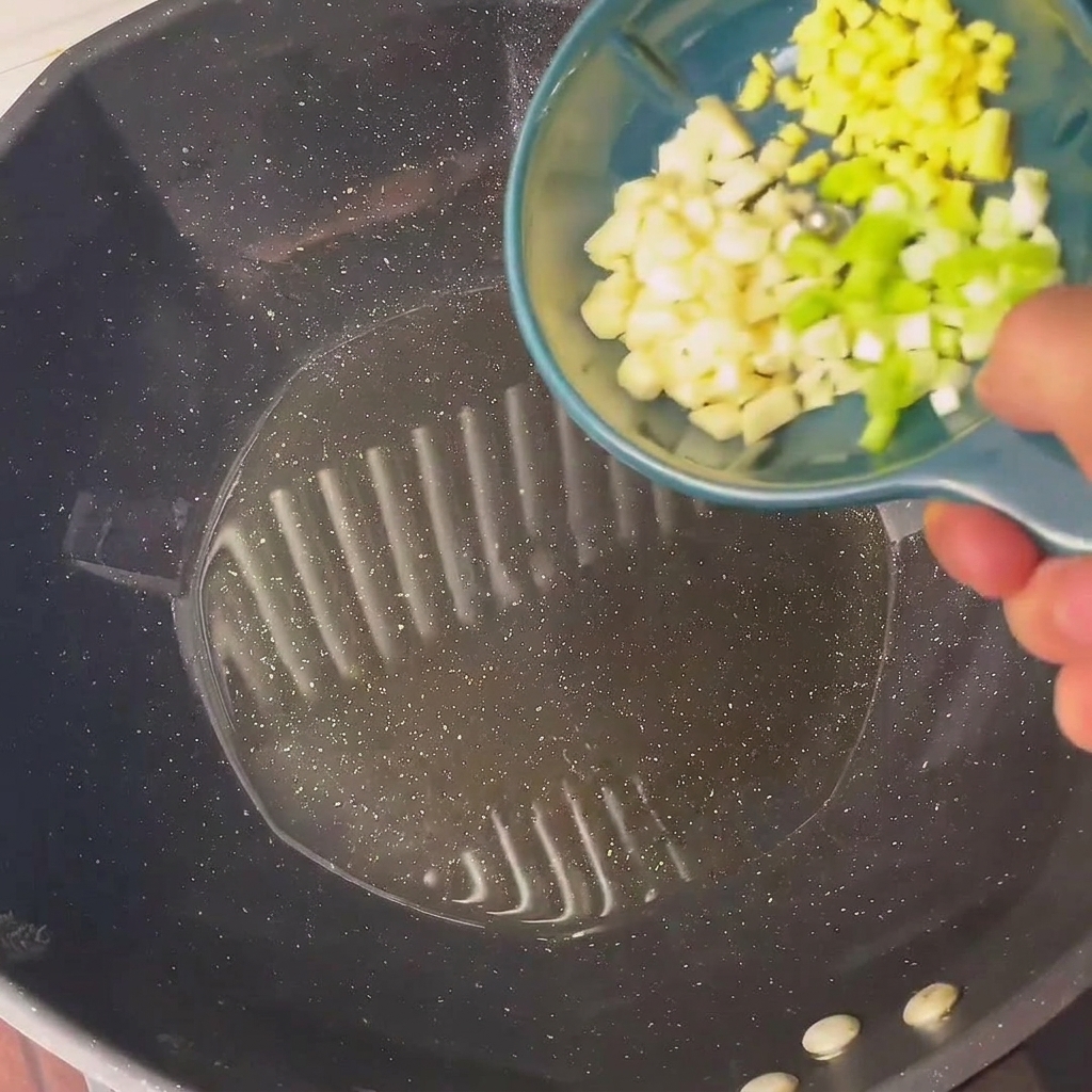 Cebolleta picada y ajo sofriéndose en aceite caliente dentro de un wok.