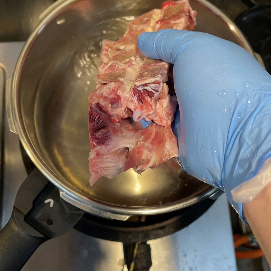 Huesos de cerdo, carcasa de pollo y manitas de cerdo hirviendo en una olla a presión para eliminar impurezas.