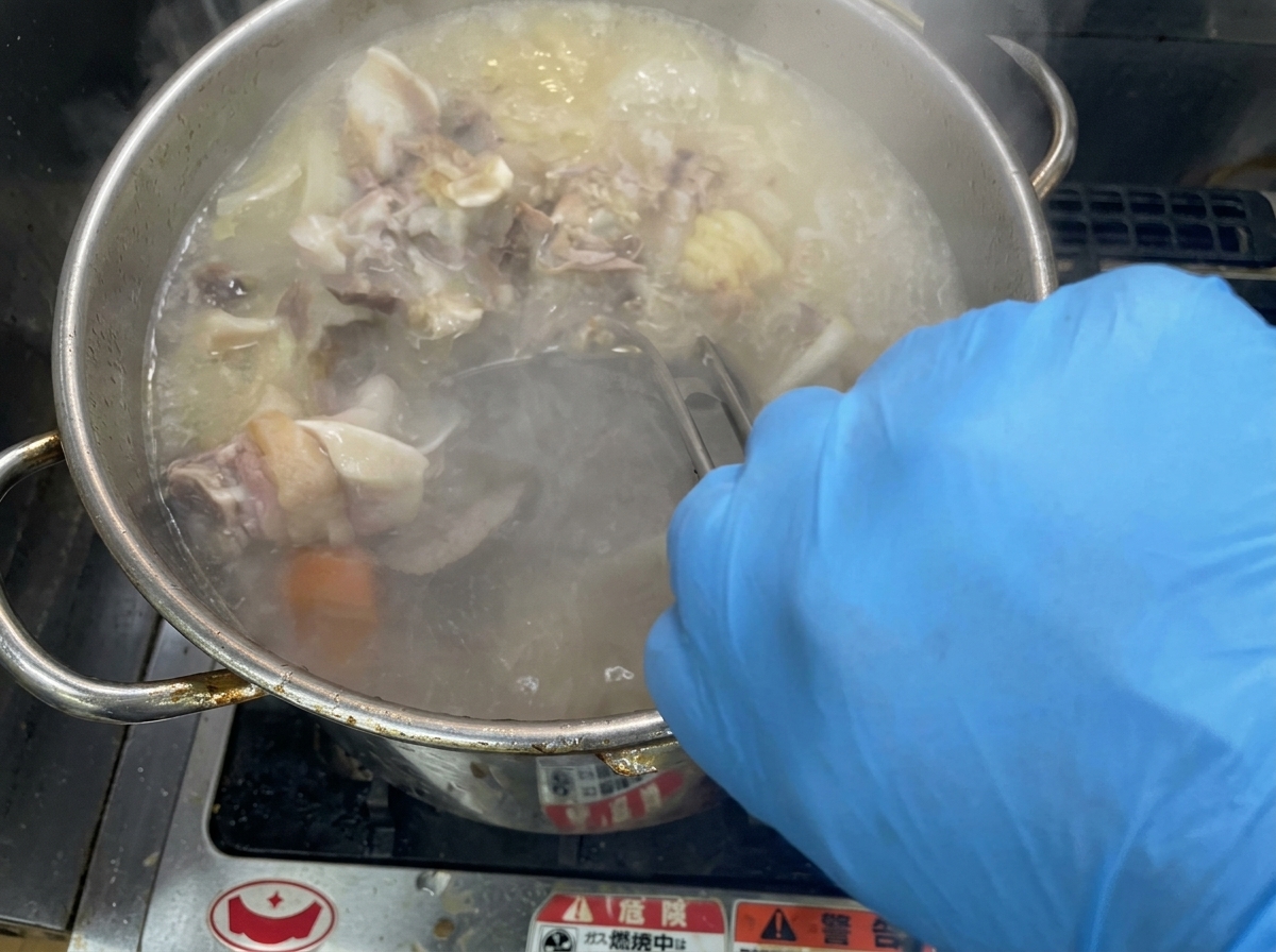 Removiendo vigorosamente un caldo burbujeante y cremoso en una gran olla de acero inoxidable.
