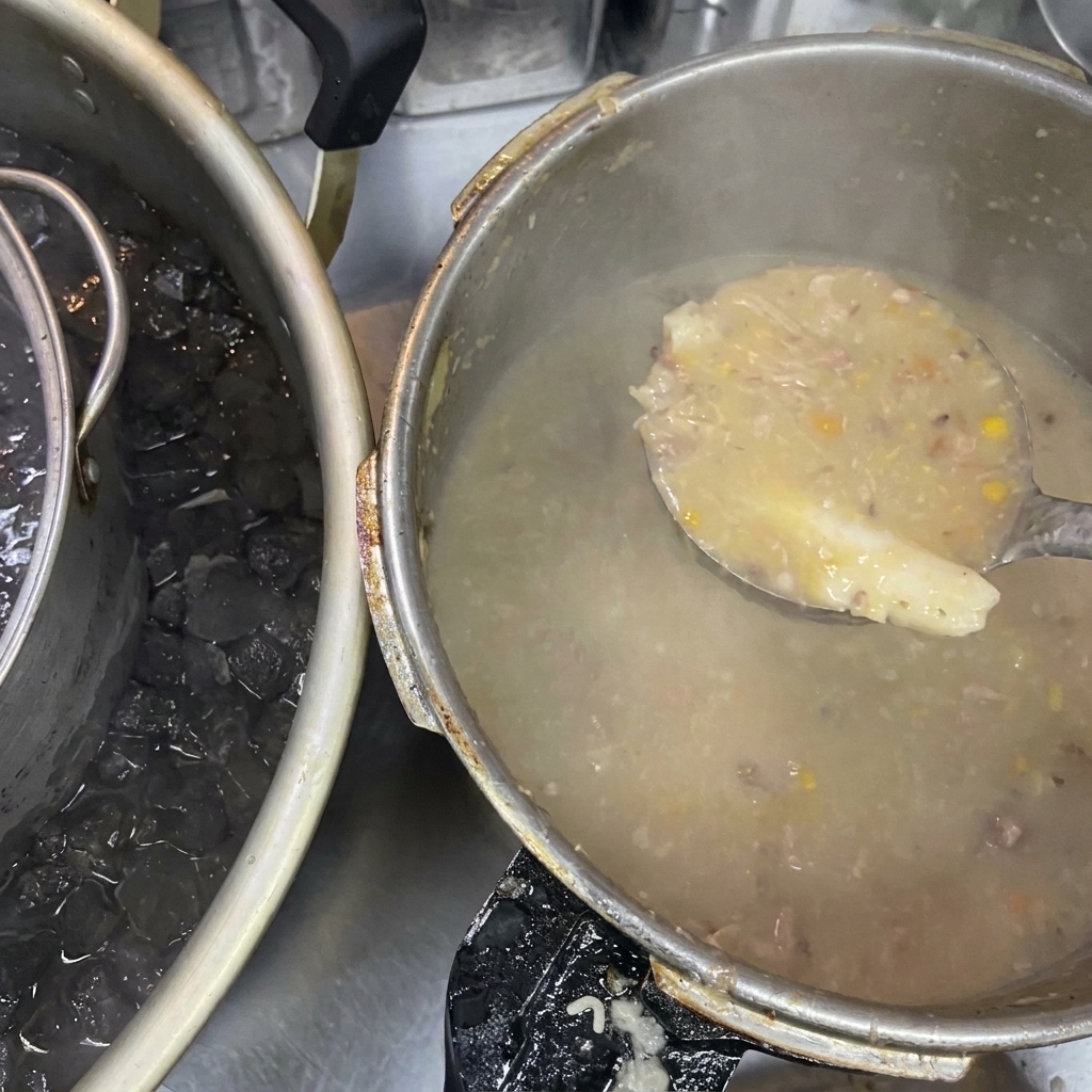 Un cucharón sosteniendo caldo espeso y turbio junto a una olla grande que descansa en un baño de hielo.