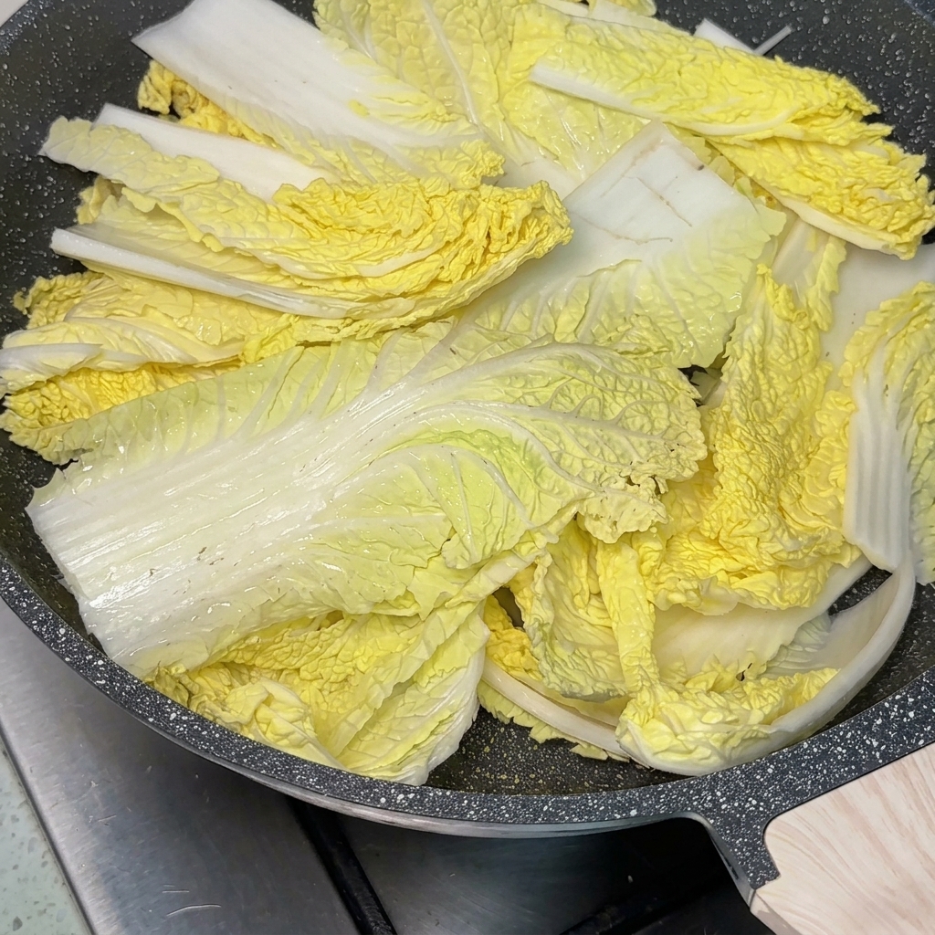 Una sartén con diversos ingredientes y una cucharada de pasta de chile en el centro, siendo rellenada con caldo.