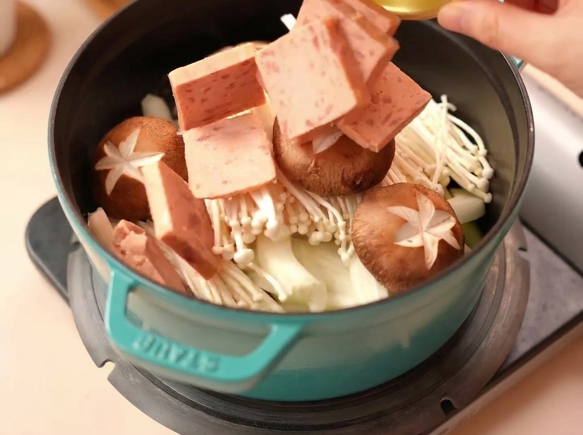 Trozos cuadrados de Spam siendo añadidos a una olla con setas shiitake.