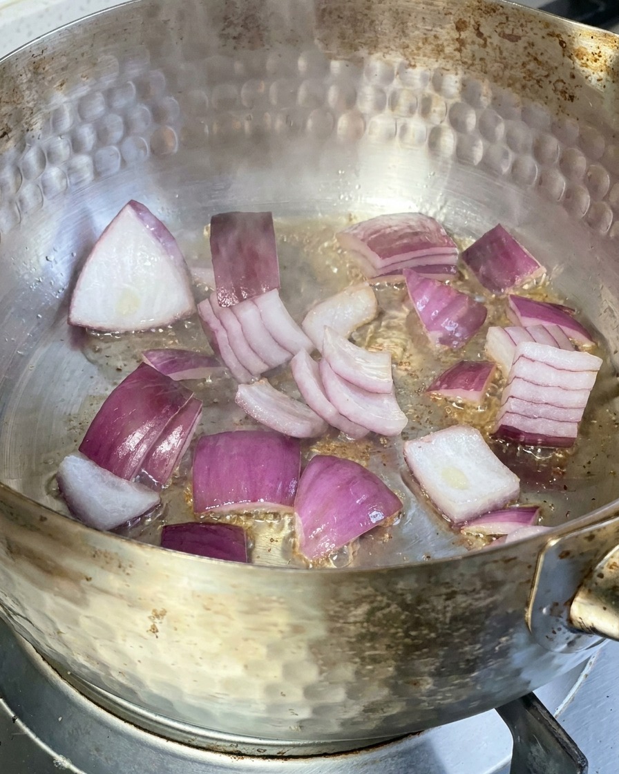 Rodajas de cebolla roja sofriéndose en una sartén metálica con aceite caliente.