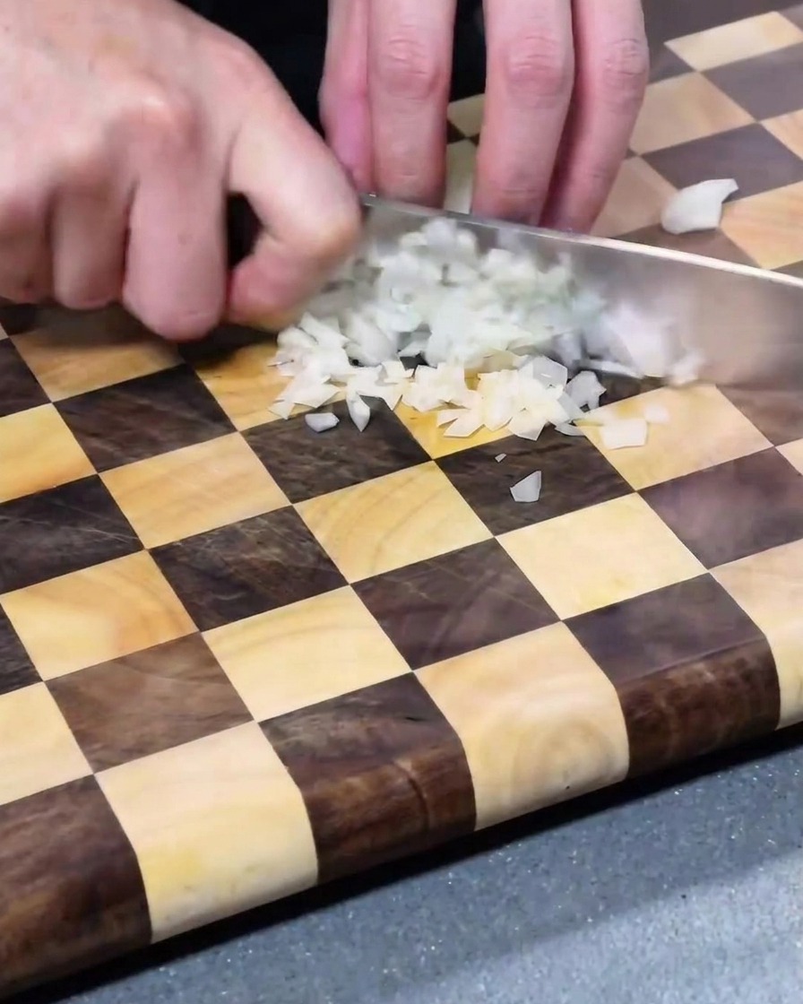 Trozos de cebolla blanca finamente picados esparcidos sobre una tabla de cortar de madera.
