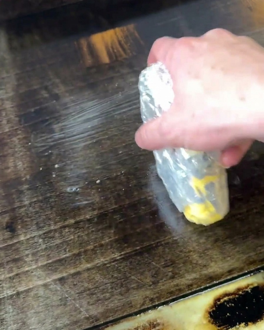 Mano derritiendo mantequilla directamente sobre una plancha caliente.