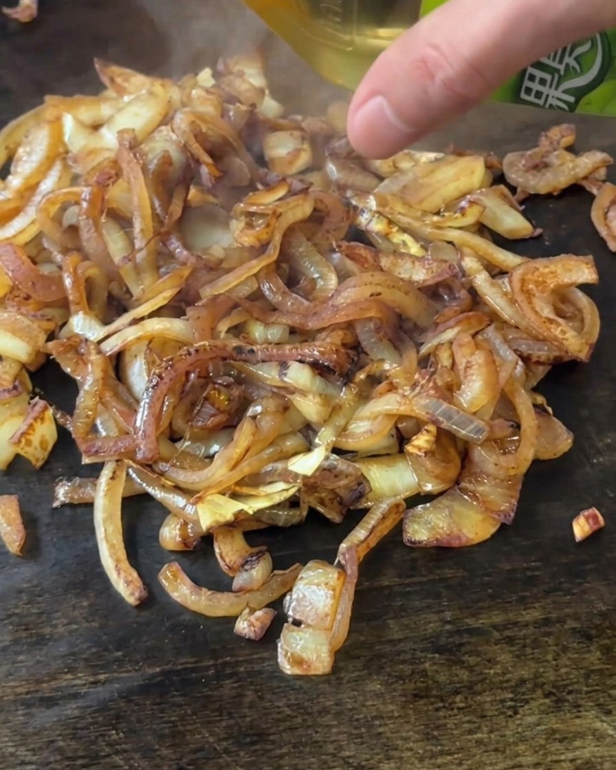 Vertiendo vinagre de manzana sobre las cebollas doradas.