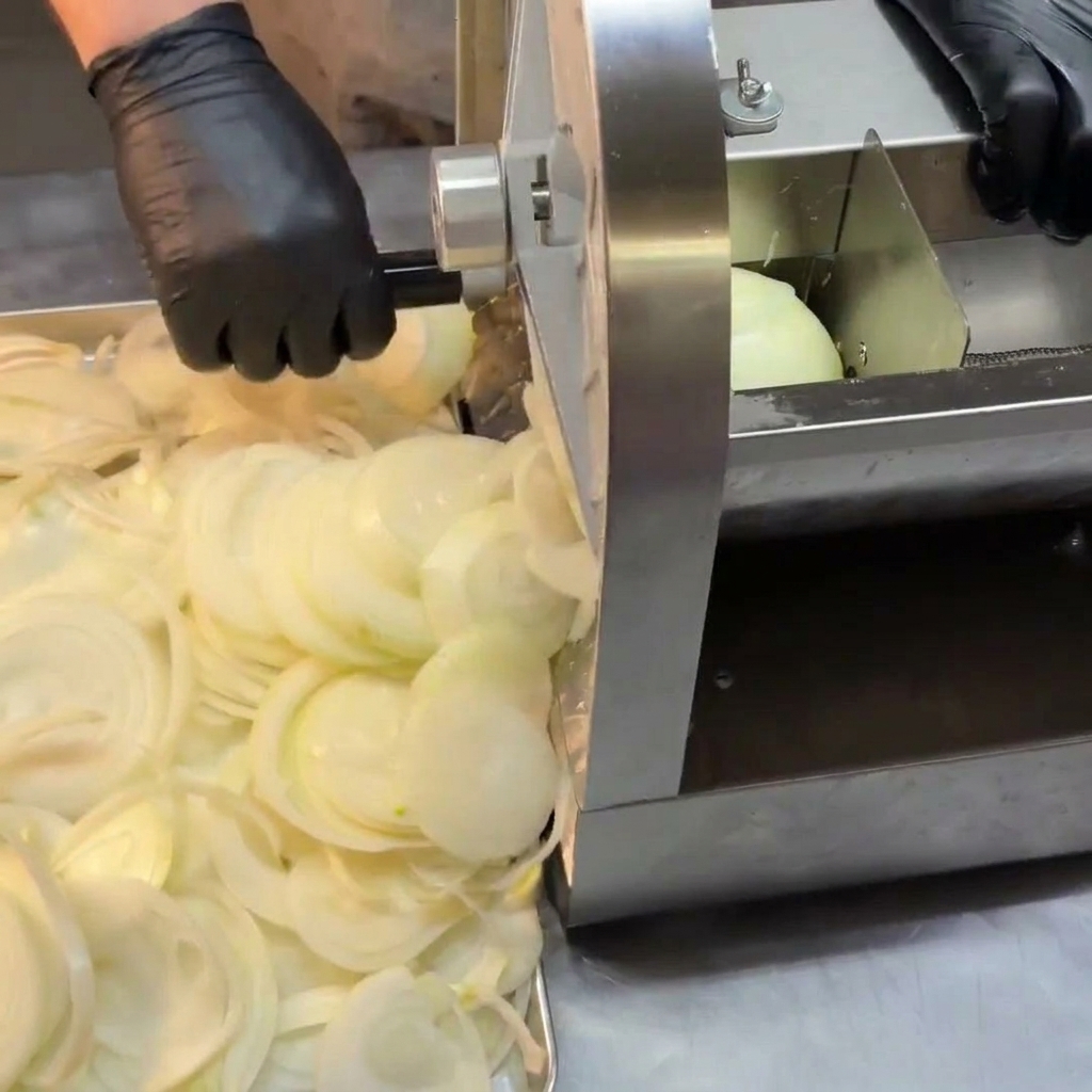 Una pila de cebollas blancas recién cortadas junto a una cortadora mecánica de acero inoxidable.