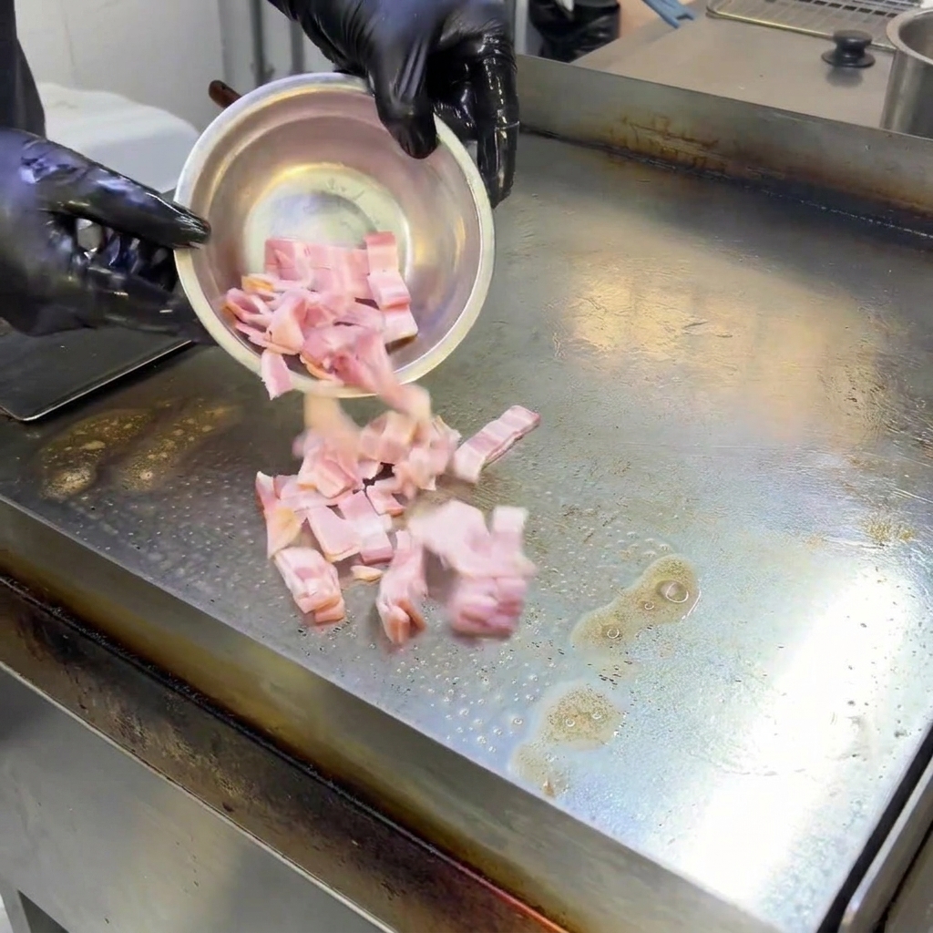 Trozos de beicon chisporroteando y friéndose en una plancha caliente, liberando su grasa.