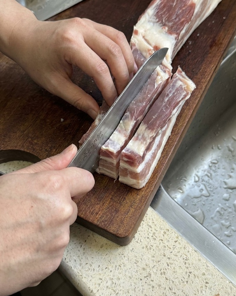 Panceta cruda siendo cortada en tiras largas y gruesas con un cuchillo de cocina afilado.