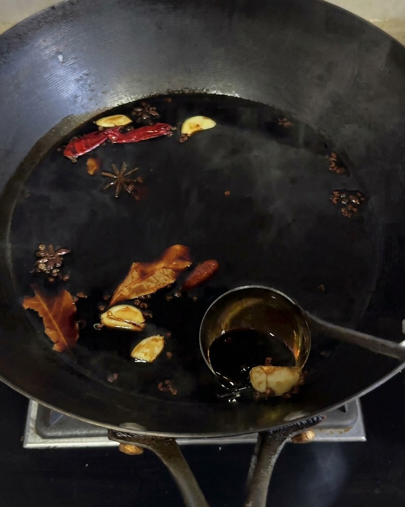 Adobo de salsa de soja oscura hirviendo a fuego lento en un wok con especias como anís estrellado y ajo.