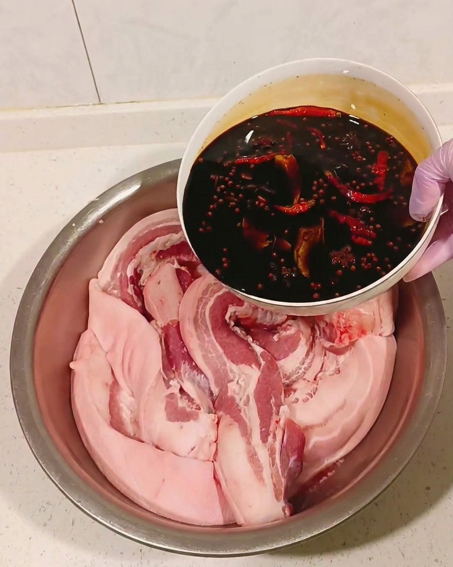 Salsa de soja especiada y enfriada siendo vertida sobre la panceta en un bol de metal.