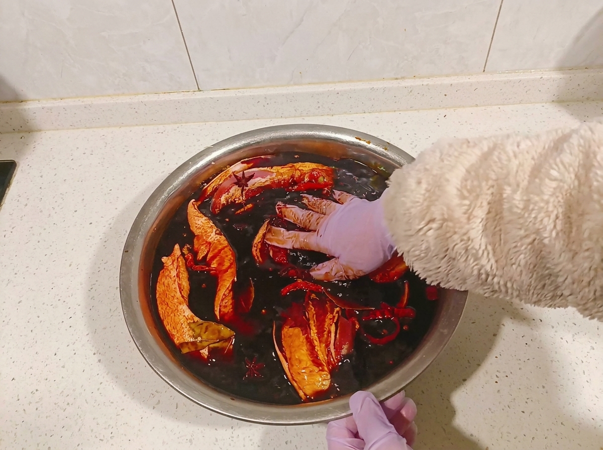 Manos con guantes girando los trozos de panceta en un bol con marinada oscura de soja.