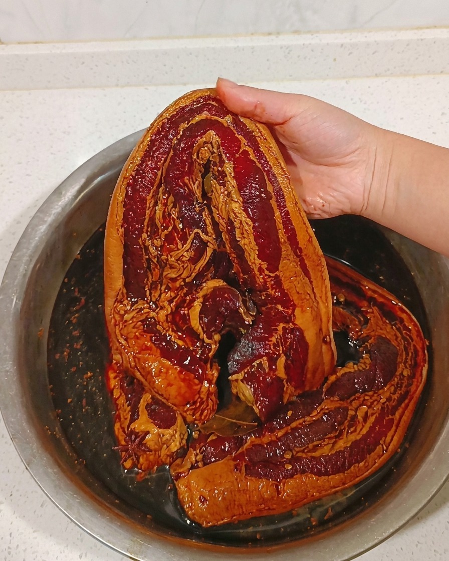 Un trozo de panceta marinada siendo enjuagado bajo un chorro de agua tibia.