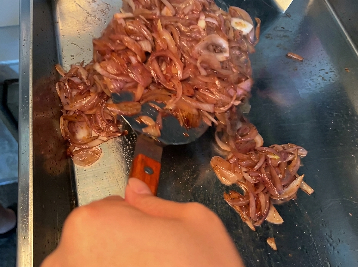 Adobo de salsa de soja oscura siendo vertido sobre trozos de panceta de cerdo cruda en un bol de metal.