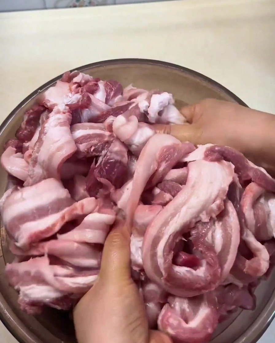 Tiras de panceta siendo masajeadas a mano con especias y condimentos en un cuenco grande.