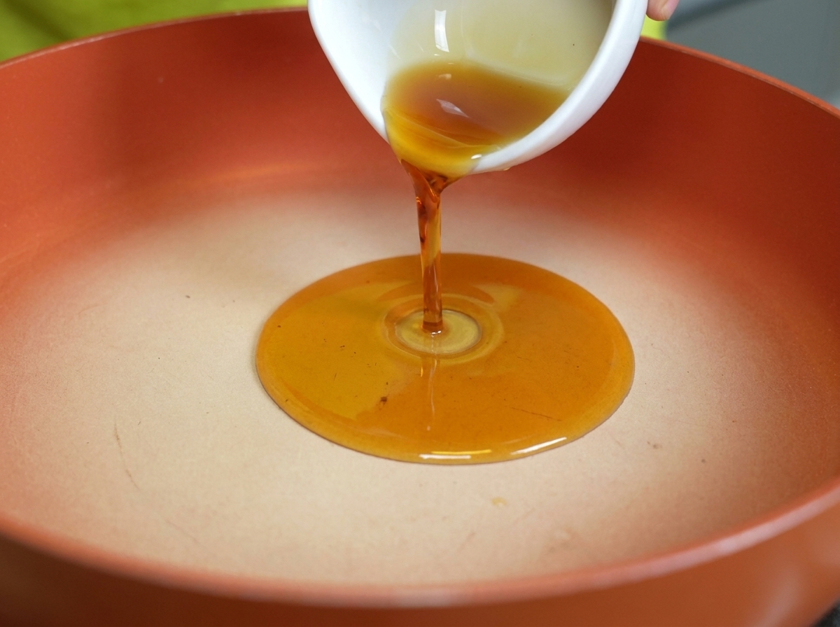 Aceite de sésamo dorado vertiéndose en una sartén caliente y limpia.