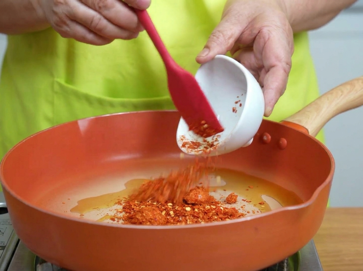 Copos de chile revolviéndose en aceite caliente brillante en una sartén.