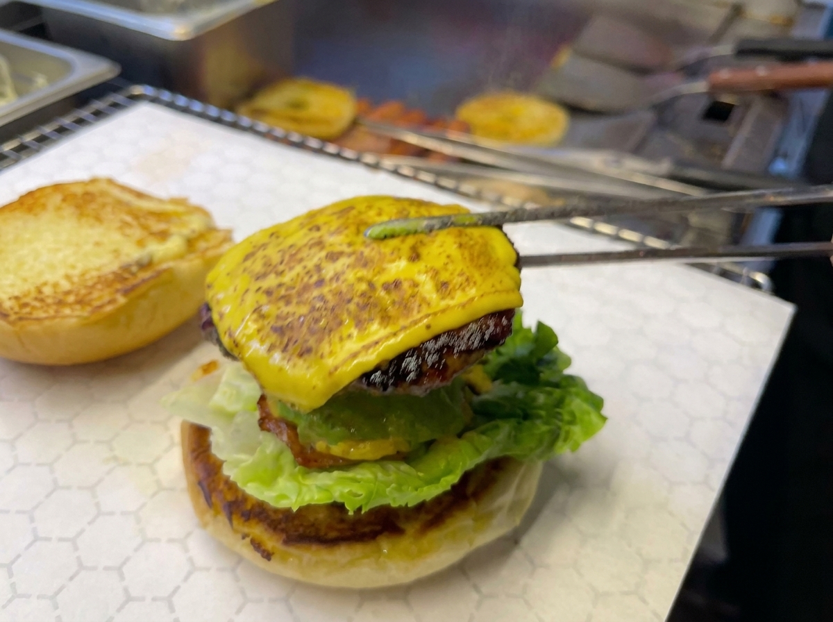 Pinzas de cocina colocando la carne con queso y piña sobre el resto de la hamburguesa.