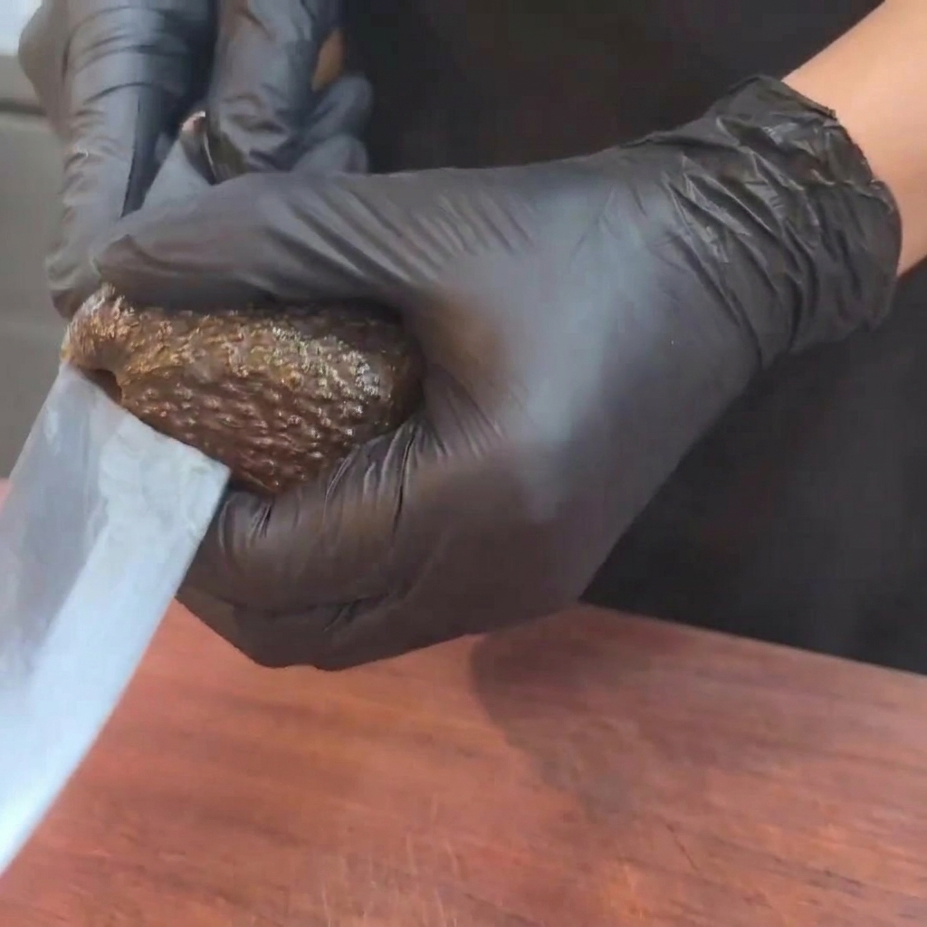 Un aguacate maduro siendo cortado por la mitad con un cuchillo sobre una tabla de madera.