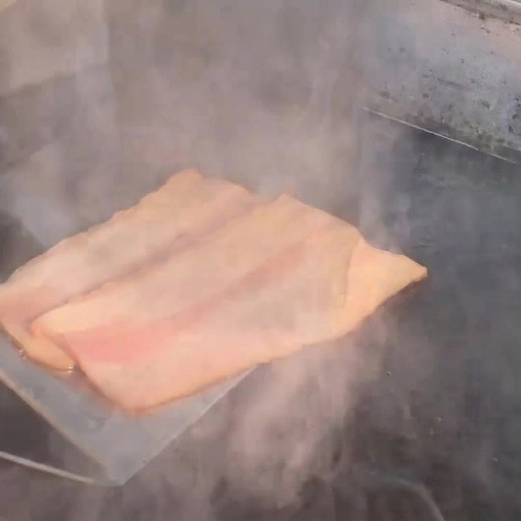 Tiras de tocino friéndose en una plancha caliente.