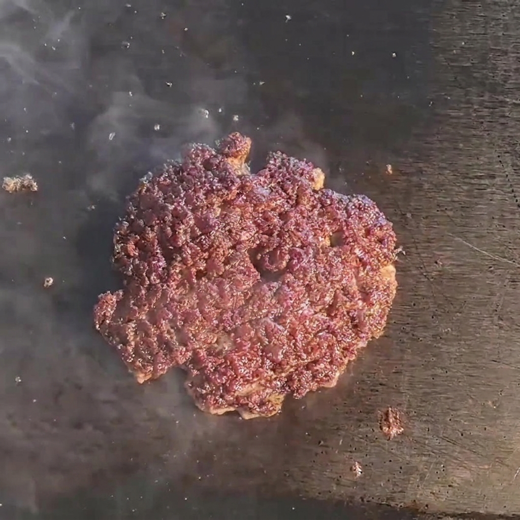 Una loncha de queso derritiéndose sobre la carne en la plancha.