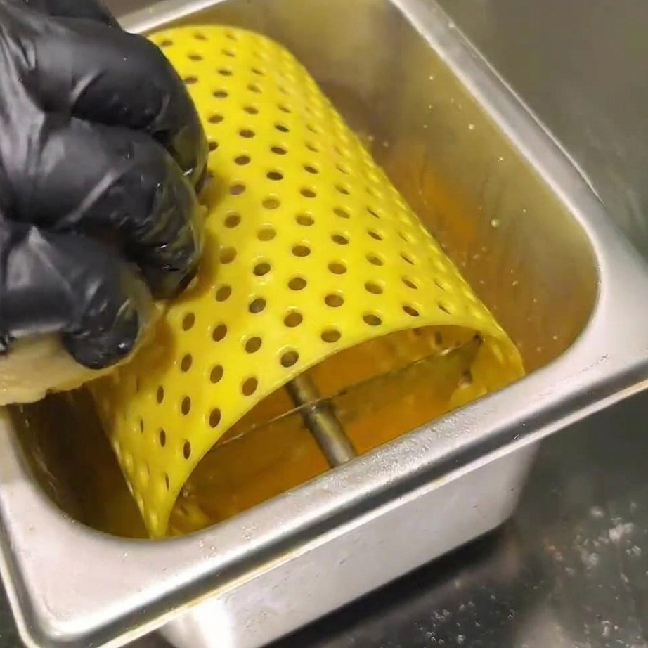 Carne de hamburguesa friéndose en una plancha caliente, siendo presionada por una espátula.