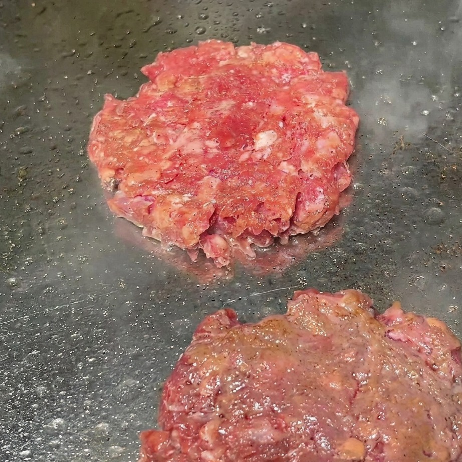 Hamburguesas en la plancha siendo espolvoreadas con pimienta negra recién molida.