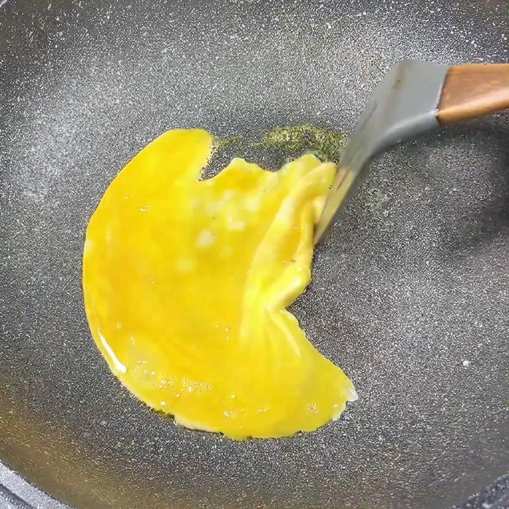 Una tortilla de huevo cocinándose en una sartén, con los bordes siendo arrastrados hacia el centro.