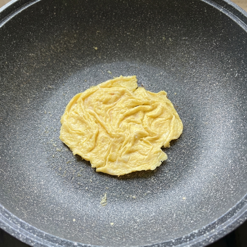 Una loncha de queso derritiéndose sobre una tortilla de huevo en una sartén.