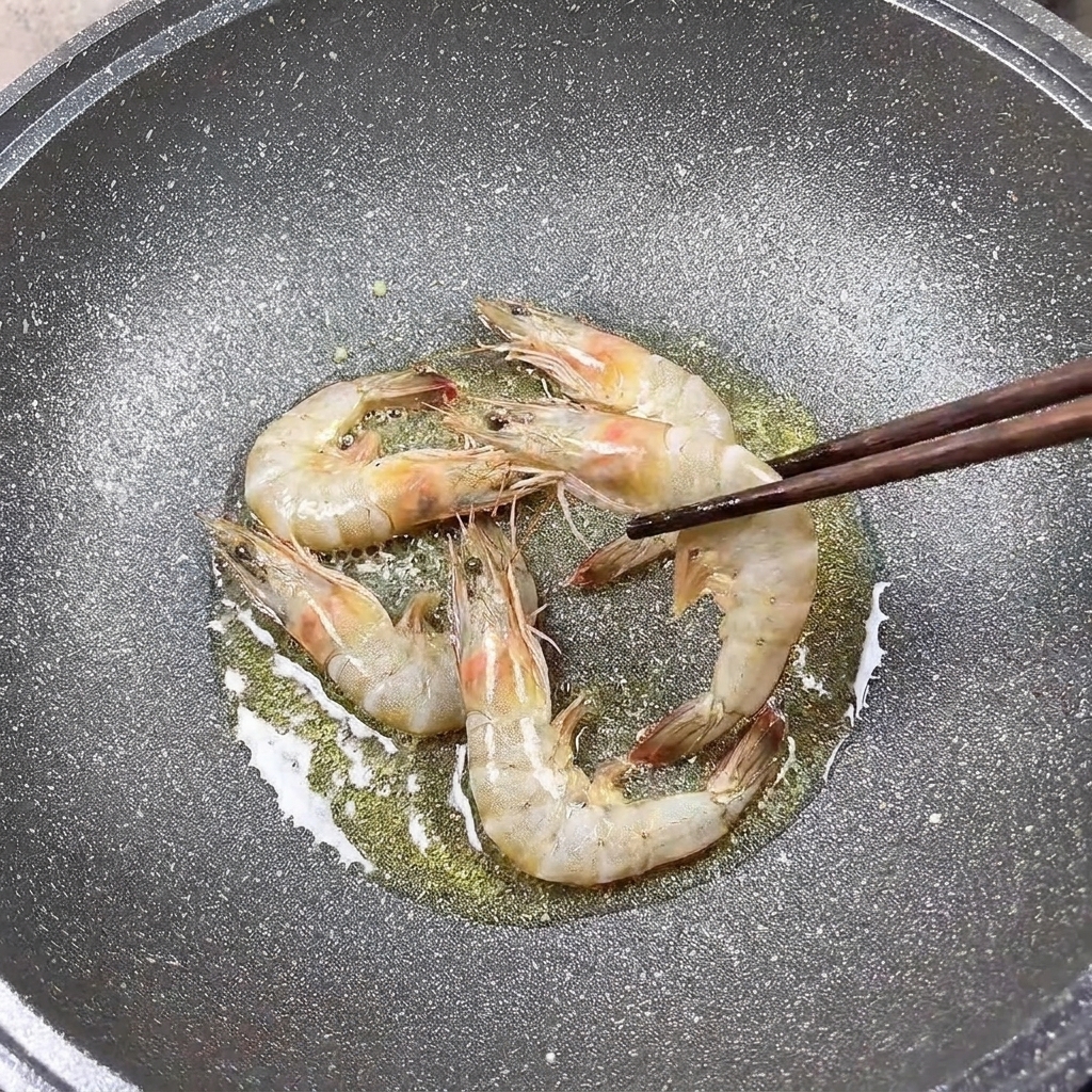 Gambas sazonadas friéndose en una sartén, siendo volteadas con palillos.