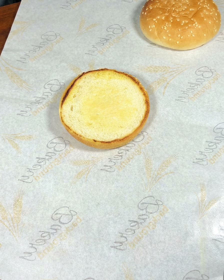 Primer plano de una hamburguesa casera siendo montada con capas de lechuga, huevo con queso, gambas salteadas y aguacate sobre un pan tostado.