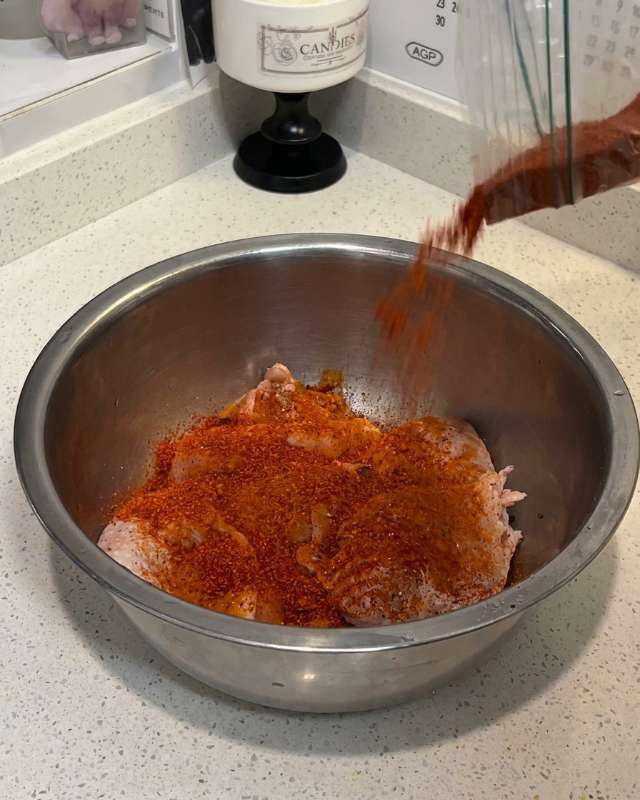 Muslos de pollo crudos sazonados con especias y leche en un bol metálico.